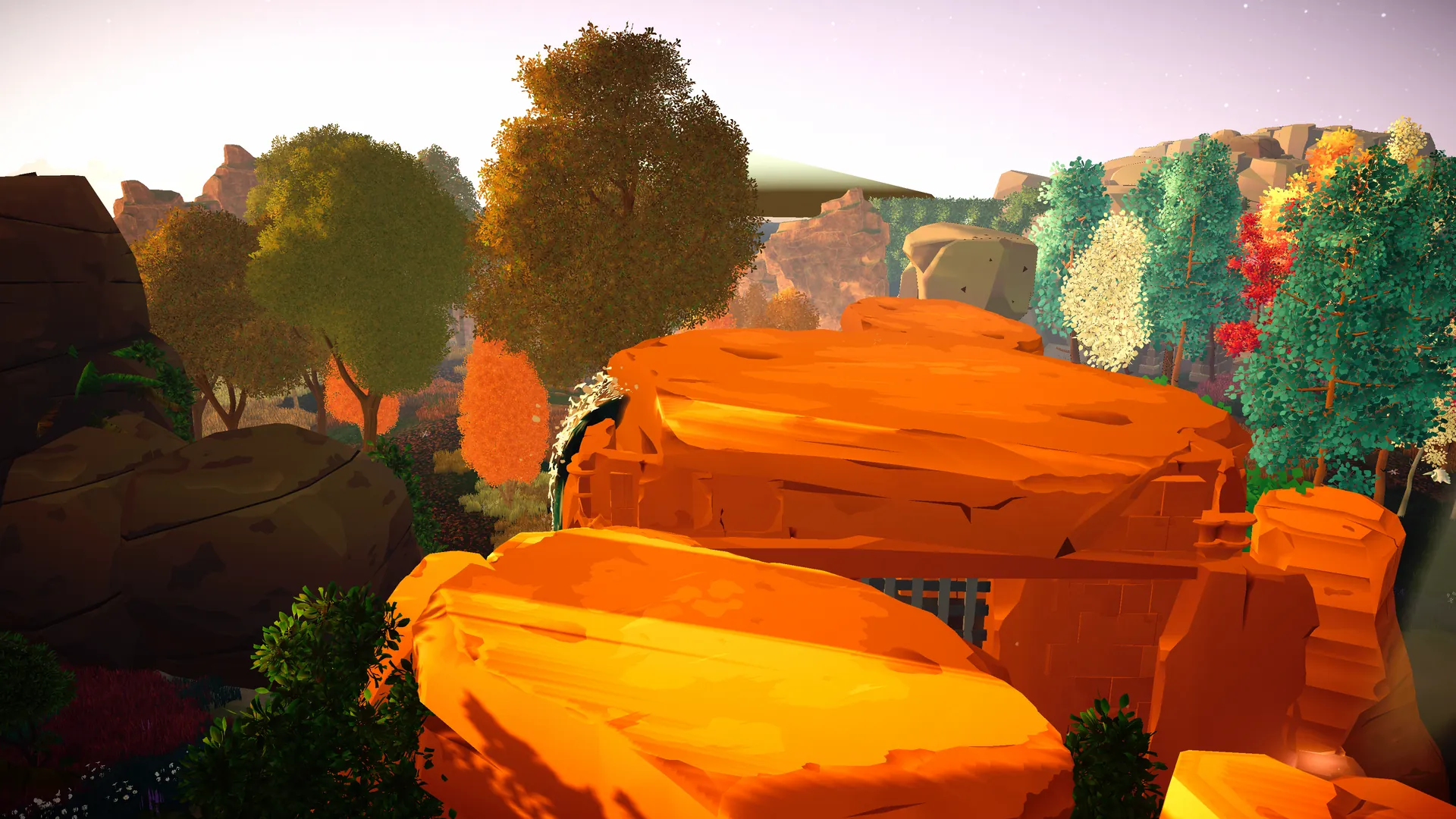 A canyon of orange rock under a golden sky, with trees on the far ridge